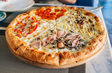 Italian pizza four seasons on a wooden board on a table in a cafe or restaurant.