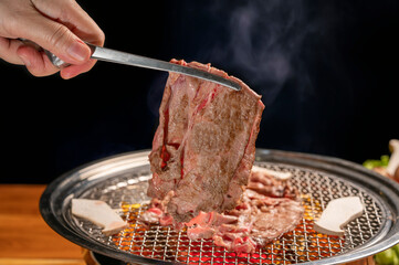 Hand using chopsticks to pick up wagyu beef on hot charcoal Asian BBQ food style, Grilled Beef...