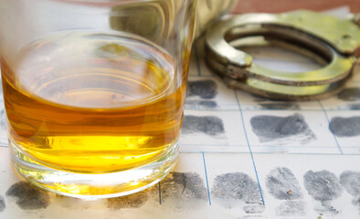 Glass of whiskey and police handcuff on fingerprint crime page file.Alcohol and law concept.