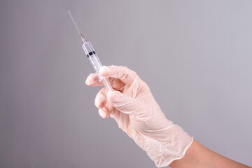 A gloved hand holds a syringe on a gray background