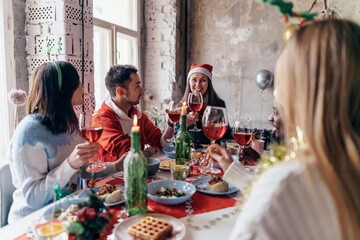 People celebrating sitting at the table, clinking glasses. Christmas or New Year eve. - obrazy, fototapety, plakaty