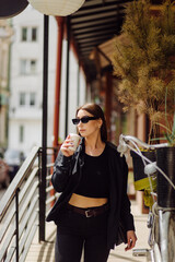 Fototapeta premium Outdoors lifestyle portrait of stunning brunette girl. Drinking coffee and walking on the city street.