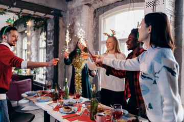 Group of people celebrating Christmas or New Year eve. Friends toasting drinks and enjoying dinner together