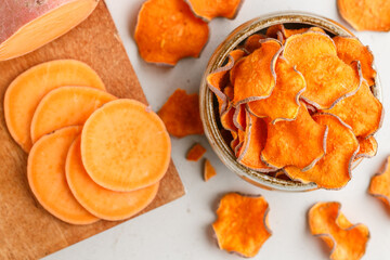 Healthy organic sweet potato chips in a bowl and fresh sweet potatoes on a wooden board. Vegetarian and vegan appetizer. Diet. A useful snack. Selective focus, top view