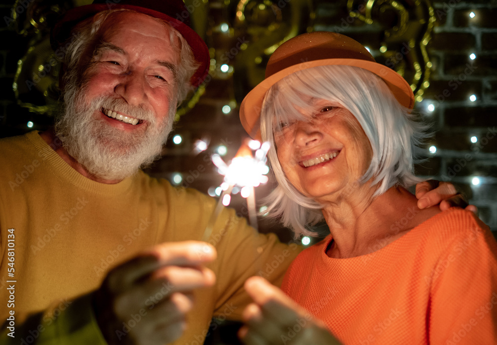 Wall mural cheerful caucasian senior couple holding sparklers celebrating new year. happy lifestyle for mature 