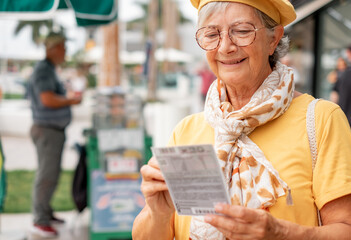 Smiling old woman checks if the lottery ticket was lucky. Attractive modern lady in yellow tries...
