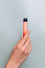 Electronic cigarette in female hand against green background.