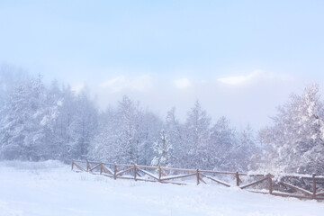 Peaks of Pirin mountains covered with snow in winter foggy day. Bansko, Bulgaria ski resort panorama with pine trees and wooden fence