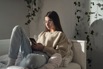 Caucasian teenage girl browsing phone while sitting on bed