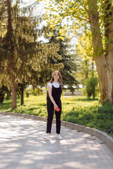 Photo of a positive cheerful teenage girl spends time in the park and using mobile phone.