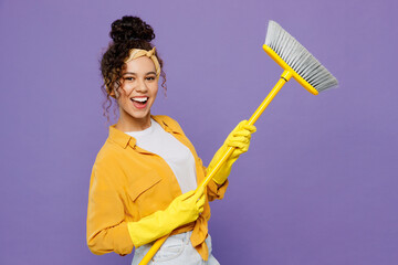 Side view young happy housekeeper woman wear yellow shirt rubber gloves tidy up hold broom sweeps...