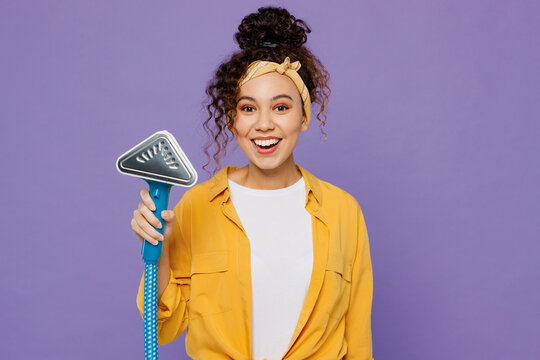 Young smiling happy fun housekeeper woman wear yellow shirt hold electrical stramer for dry-cleaning and ironing isolated on plain pastel light purple background studio. Housework tidying up concept.