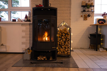 Black metal stove fireplace with wood in a woodpile - the interior of a private village house. Heating and heating of the house with firewood, the heat of the fire from the hearth. - obrazy, fototapety, plakaty