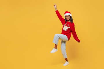 Fototapeta na wymiar Full body side view merry little kid teen girl 13-14 years old wear red xmas sweater with deer Santa hat posing raise up hand isolated on plain yellow background. Happy New Year 2023 holiday concept.