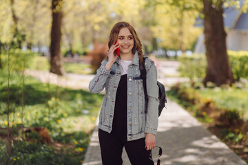 Photo of a positive cheerful teenage girl spends time in the park and using mobile phone.