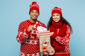 Merry young fun couple two man woman wear red Christmas sweater Santa hat posing hold stocking with...