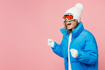 Side view snowboarder excited woman wear blue suit goggles mask hat padded jacket pov holding ski poles isolated on plain pastel pink background. Winter extreme sport hobby weekend trip relax concept. © ViDi Studio