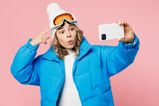 Snowboarder woman wear blue suit hat ski jacket do selfie shot on mobile cell phone show goggles mask isolated on plain pastel pink background. Winter extreme sport hobby weekend trip relax concept.