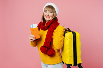 Traveler elderly woman 50s in sweater Santa hat hold passport ticket bag isolated on plain pink background Tourist travel abroad in free time rest getaway. Air flight trip concept Happy New Year 2023.