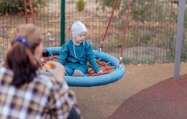 Cute Little boy with down syndrome in a funny hat with his mother, swinging on a swing, soap bubbles