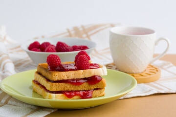 Toast with raspberry jam and cup of tea on beige table.