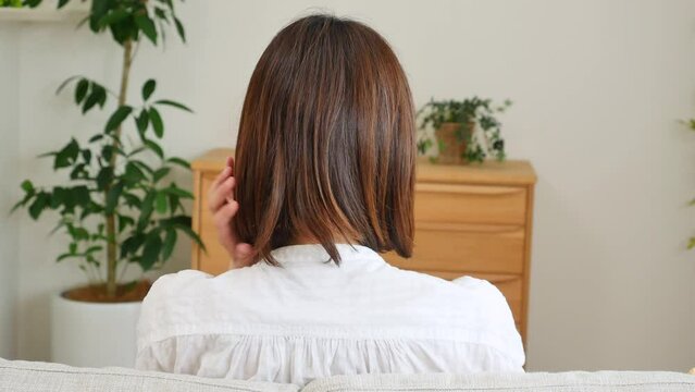 家で髪の毛を手ぐしする女性の後ろ姿
