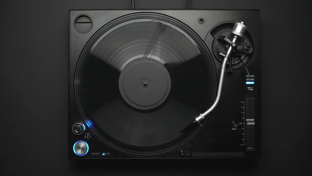 DJ turntable playing vinyl record with music in flat lay 4K video clip. Retro disc jockey player filmed directly from above on a black background. 