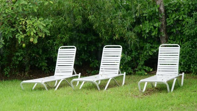 Slow motion rain drops falling on ground against bushes on back yard. Sunbed lounger in tropical garden. Rainy weather on summer day. Downpour. Green threes. Nature. High quality 4k footage