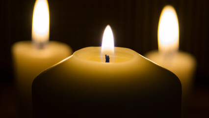 three lit candles in dark. One big candle in the foreground and two candles in the background