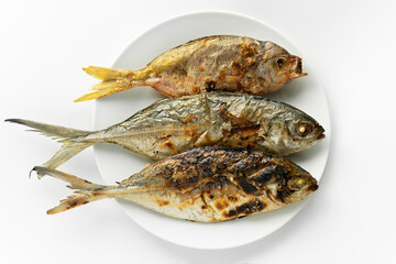 Top down view or flatlay closeup served Grilled burn three fish in a white round plate on isolated...