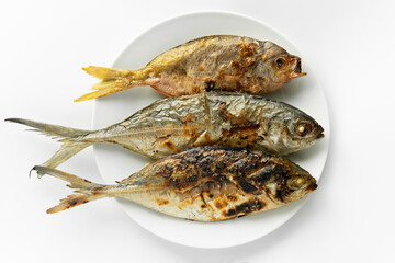 Top down view or flatlay closeup served Grilled burn three fish in a white round plate on isolated clean white background. Food rich in omega-3 fatty acids