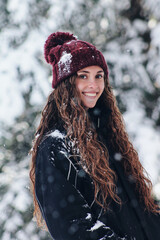 Fototapeta na wymiar portrait of a happy woman on a snowy day in winter. Woman bundled up in a hat and anorak. Snowy cold forest. Snow flakes. Enjoying winter and snow. Caucasian woman with long hair and hat.