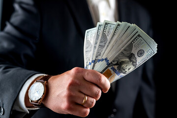 businessman in a shirt and jacket counts hundred dollar bills in front of his chest.