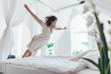 Woman jumps on the bed as if in flight - 546824348
