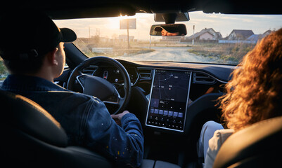 Rear view inside the car. Driver and passenger travelling by electric car with modern user interface with touch screen on dirt road. Male chauffeur riding on terrain using navigation system.