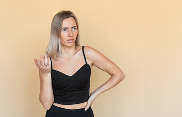 Naklejka premium Serious young woman with freckles gestures hand, looking frowning and thoughtful, stands over beige background