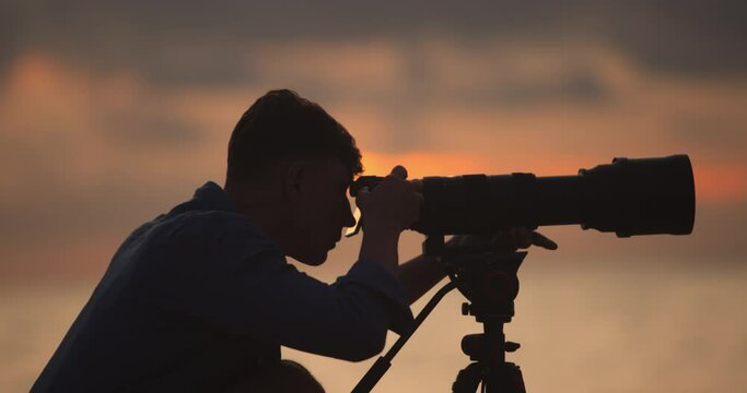 Silhouette of a man photographer with professional camera and long lens and tripod photographs a beautiful sunset 4K