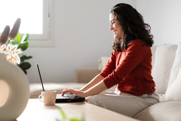 Happy young woman using laptop sitting on the couch