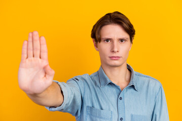 Portrait of casual man showing stop sign isolated over yellow bright color background