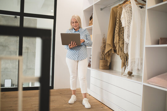 Woman with laptop in hands choosing clothes in a wardrobe