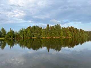 Forest trees reflection on the lake surface, lake mirror, quiet peaceful atmosphere, cloudy blue sky
