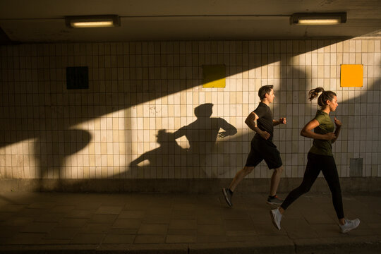 Young man and woman jogging by tiled wall