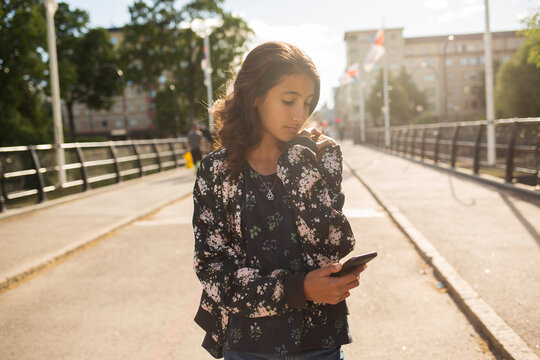 Girl holding smartphone while walking on bridge