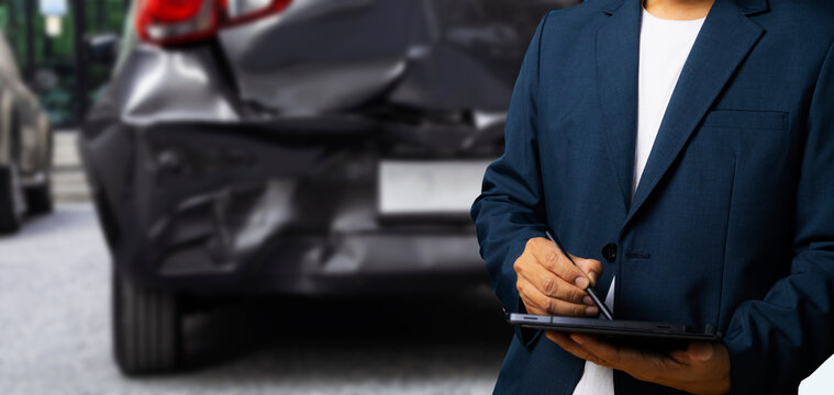 Side view of insurance officer writing on tablet while insurance agent examining black car after accident.