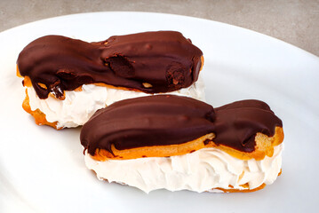 two freshly made chocolate eclairs on white plate with copy space