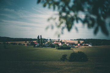 tree branches In the foreground and a village On the horizon a summer landscape