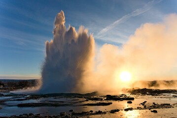 Landscape of splashing Strokkur fountainwith  snowy glacier in the water, Iceland at sunrise