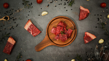 Raw striploin beef meat chopped in cubes with pepper, sea salt, rosemary and spices on black stone...