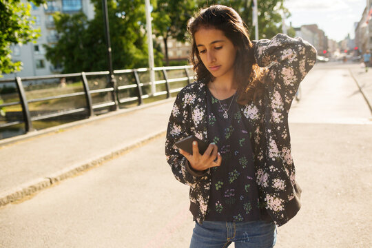 Girl holding smartphone while walking on bridge