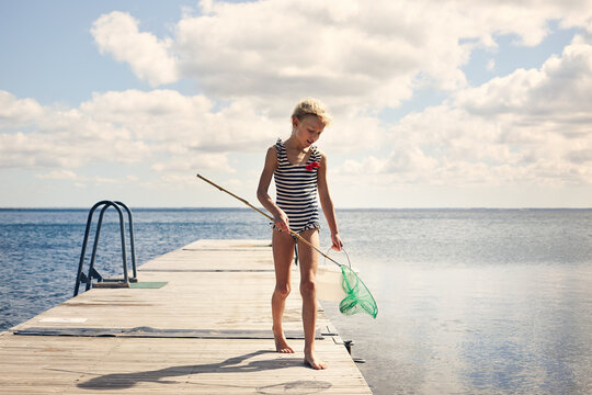 Girl in striped swimsuit with fishing net on jetty